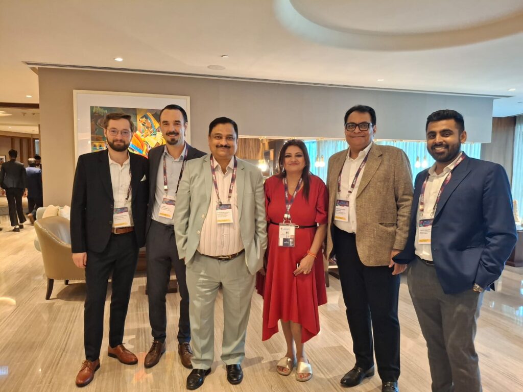 Group of six delegates, including a woman in a red dress, posing together in a hotel lobby at Purify 25