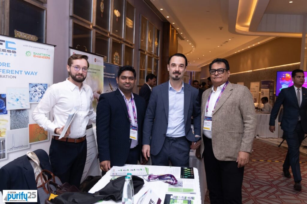 Four delegates smiling beside the Sanitech Engineers and SFE Process stall in the Purify 25 exhibition hall
