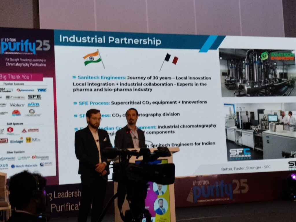 Two presenters standing before the Industrial Partnership slide on Sanitech Engineers and SFE Process
