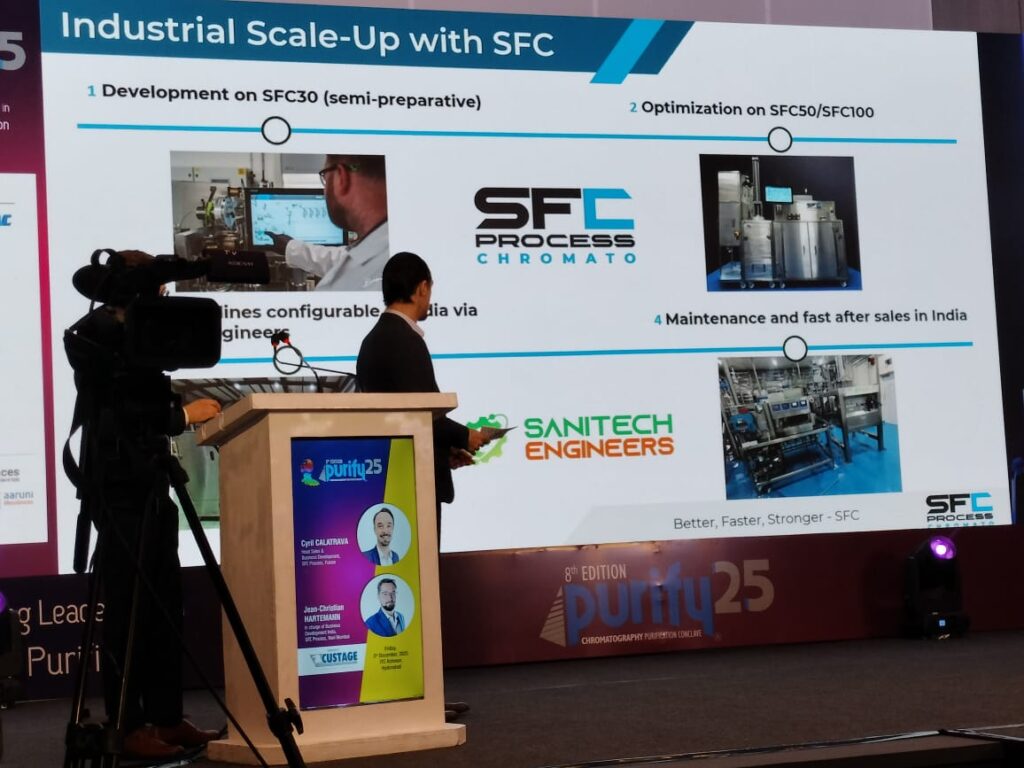 Presenter at the podium beside a slide on scale-up with SFC, showing SFC30 and SFC100 systems