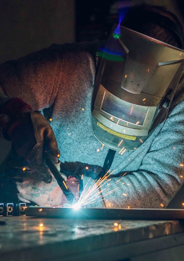 Worker in a factory welding metal with welding machine while wearing a protective gear. Yellow sparks fly in sides during working with steel at workshop. Dangerous work concept.